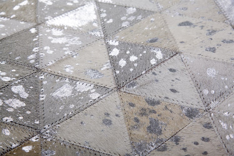 Detailaufnahme eines Patchwork-Teppichs aus dreieckigen Kuhfellelementen mit silbernem Metallic-Druck und Zickzack-Nähten.