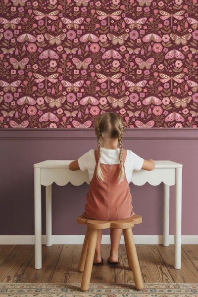 Mädchen sitzt an einem Kindertisch vor einer Wand mit Blumen- und Schmetterlingstapete