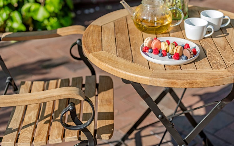 Holz Gartentisch mit Stuhl, Teekanne, Tassen, Macarons und Beeren auf einem Teller