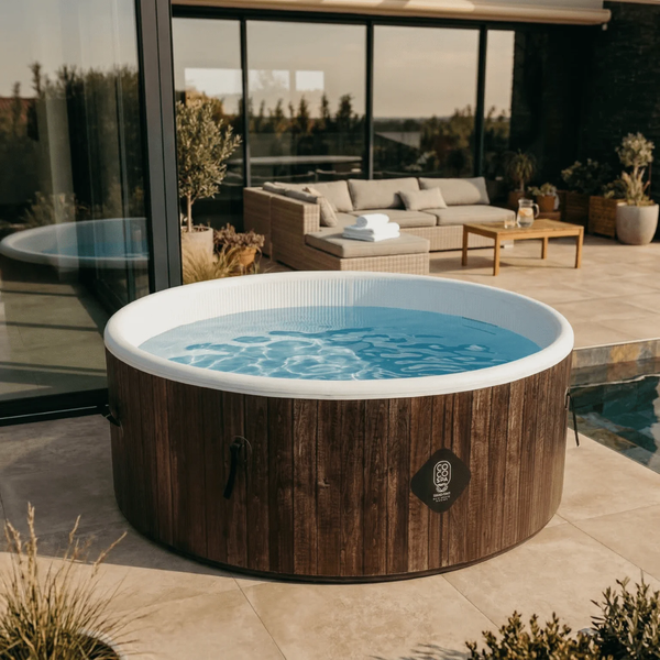 Runder Whirlpool mit Cosy Spa Logo in dunkler Holzoptik auf einer Steinterrasse mit modernen Gartenmöbeln und Glasfronten im Hintergrund.