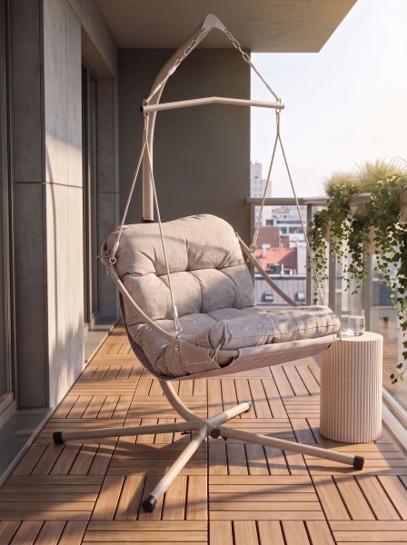 Moderner Hängesessel mit Gestell und Polster auf einem hellen Balkon mit Holzboden, Pflanzen und Stadtblick.