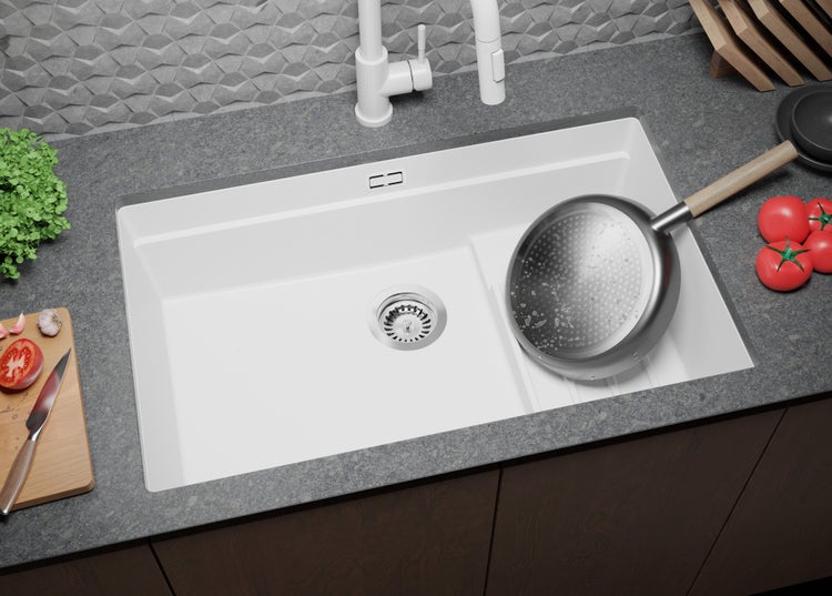 Weißes Spülbecken mit Abtropffläche, Armatur, Schneidebrett und Kochutensilien auf einer Küchentheke.