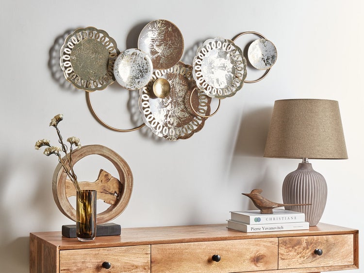 Dekorative Wanddeko aus Metall über einer Holzkommode mit Lampe, Vase und Büchern