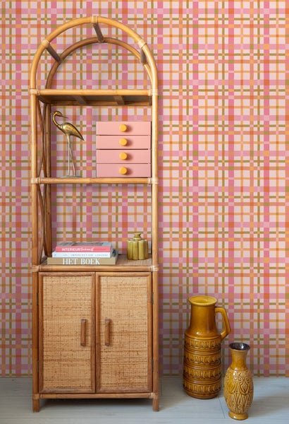 Karierte Tapete in Pink und Orange hinter einem Bambusregal mit Dekorationsartikeln wie Vasen und Buechern.