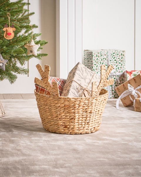 Weidenkorb mit Weihnachtsgeschenken neben einem Weihnachtsbaum