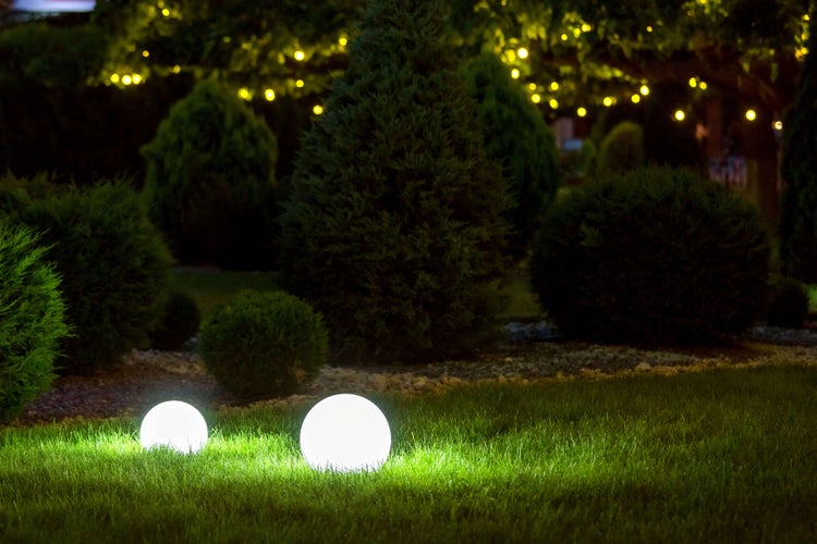 Beleuchteter Garten mit kugelförmigen Lampen und Sträuchern