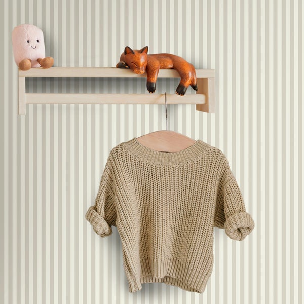 Wandregal aus hellem Holz mit Kleiderstange vor gestreifter Tapete, dekoriert mit Spielzeug und einem Strickpullover auf einem Holzkleiderbügel.