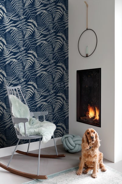 Wohnzimmer mit blauer Farnmuster-Tapete, Kamin, Schaukelstuhl und Hund