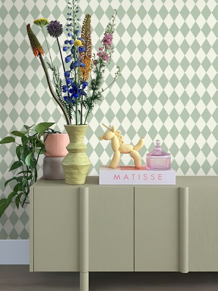 Dekoratives Arrangement auf einem Sideboard mit Blumen, Pflanze und Ziergegenständen vor einer gemusterten Tapete