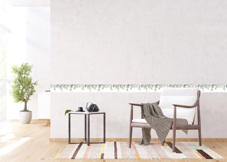 Helles, modernes Zimmer mit einer Tapetenbordüre mit grünem Blättermotiv an der Wand, Holzarmsessel, Beistelltisch und gestreiftem Teppich.