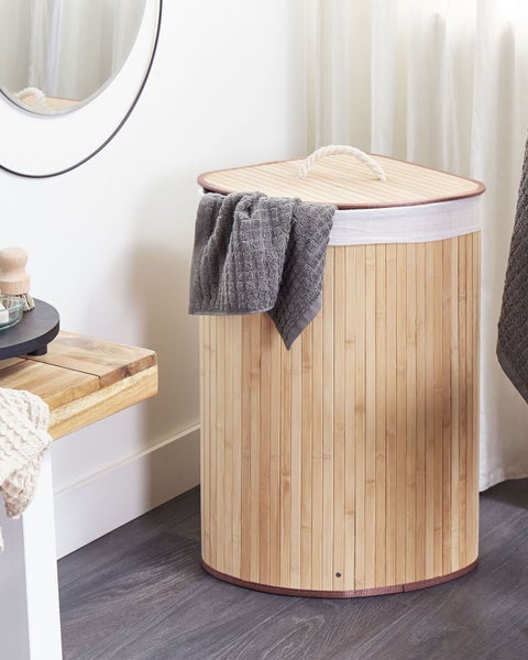 Wäschekorb aus Bambus mit Deckel und Seilgriff in einem hellen Badezimmer neben einer Holzbank.