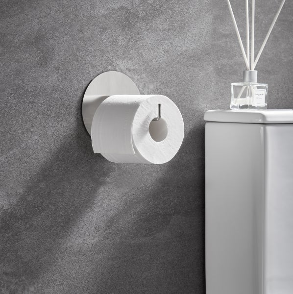 Wandmontierter Toilettenpapierhalter aus Metall mit Toilettenpapierrolle an einer strukturierten Wand neben einer Toilette.