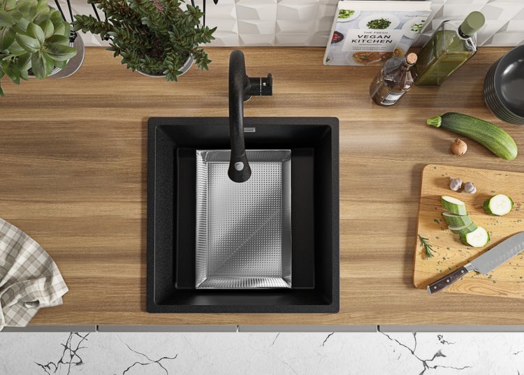 Draufsicht auf eine Küchenspüle mit Abtropfschale, Armatur, Schneidebrett mit Zucchini, Kräutern und Kochbuch auf einer Küchentheke