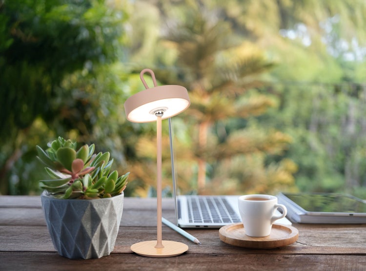 Szene mit einer Schreibtischlampe, einer Topfpflanze, einer Kaffeetasse, einem Laptop und einem Tablet auf einem Schreibtisch