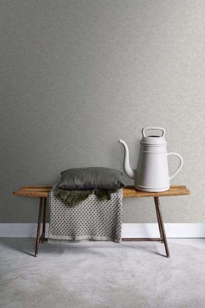 Dekorative Szene mit Bank, Kissen, Decke und Gießkanne vor einer Wandtapete