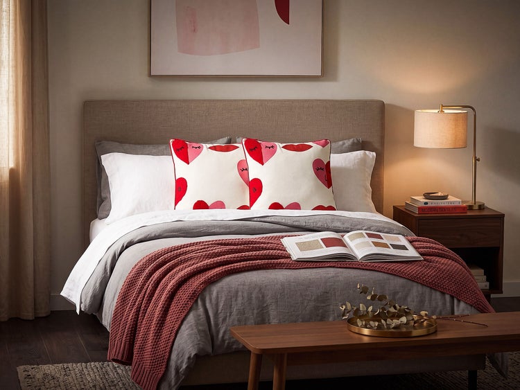 Modernes Schlafzimmer mit Doppelbett, gemusterten Herzkissen, grauer Bettwäsche, Überwurfdecke und Nachttischlampe in gemütlicher Atmosphäre.