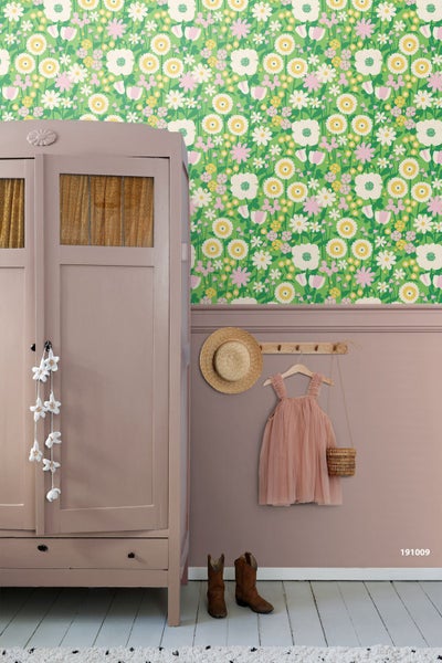 Kinderzimmer mit bunter Vliestapete im Blumenmuster, altrosa Wandleiste, passendem Kleiderschrank aus Holz und dekorativen Elementen.