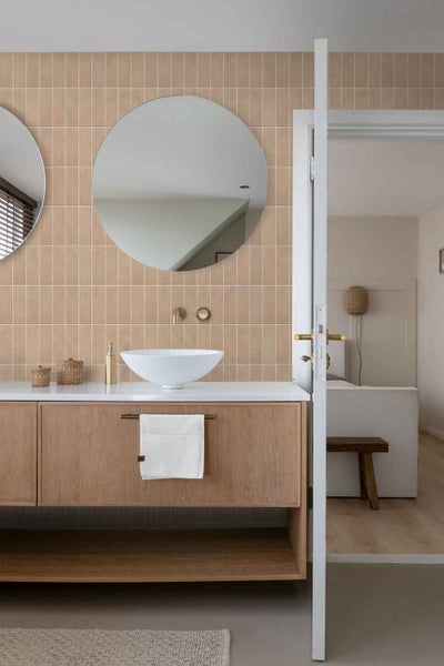 Modernes Badezimmer mit rechteckigen Wandfliesen, einem runden Spiegel und einem Holzwaschtisch mit aufgesetztem Waschbecken.