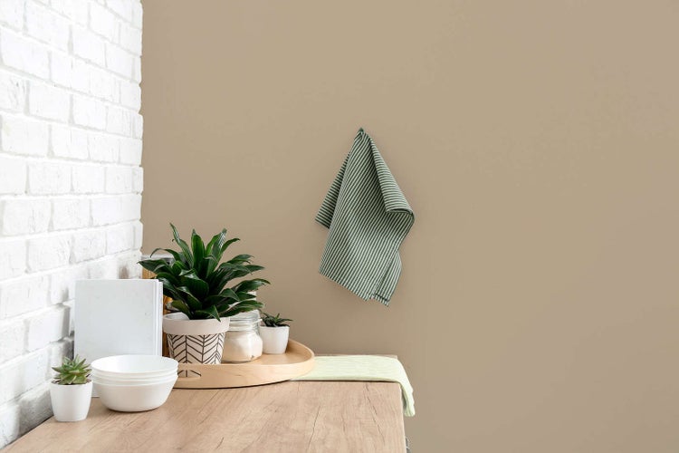 Moderne Kücheneinrichtung mit sandfarbener Wandfarbe, weißer Backsteinwand, Holz-Arbeitsplatte, Zimmerpflanzen und Küchenutensilien.