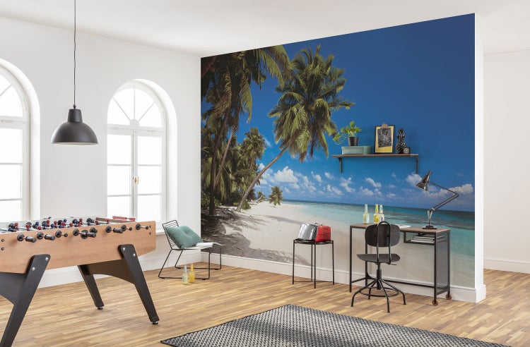 Innenraum mit Fototapete, die einen Strand mit Palmen darstellt, sowie Möbeln wie Tischfußball und Schreibtisch