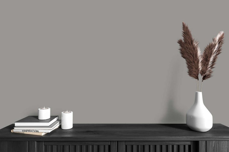 Modernes Interieur mit grauer Wandfarbe, dunklem Sideboard aus Holz, weißer Vase mit Pampasgras, Kerzen und Büchern.