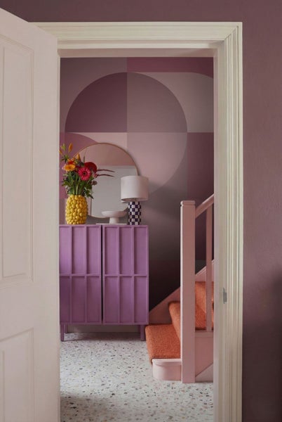 Fluransicht mit Kommode, Spiegel, Lampe, Blumen, Tapete und Treppe