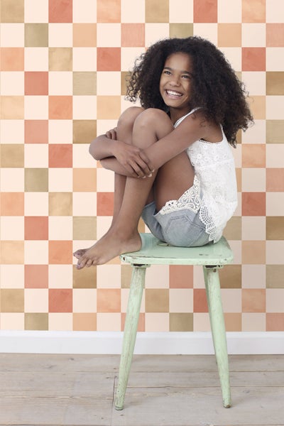 Mädchen sitzt vor einer Wand mit quadratischem Muster auf einem Hocker