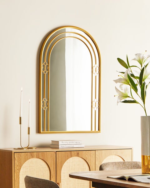 Dekorativer Spiegel mit goldenem Rahmen, auf einer Kommode platziert, neben Kerzenständer und Blumenvase.