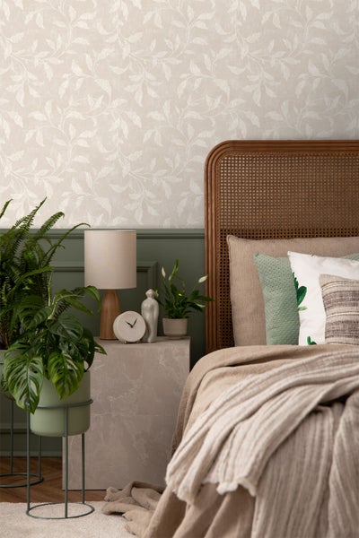 Schlafzimmer mit Wandtapete mit Blattmuster, Bett mit geflochtenem Kopfteil und Nachttisch mit Zimmerpflanzen