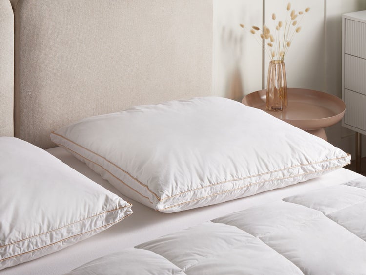 Bett mit weißen Kopfkissen und einer Steppdecke, einem gepolsterten Kopfteil und einem Beistelltisch mit Blumenvase.