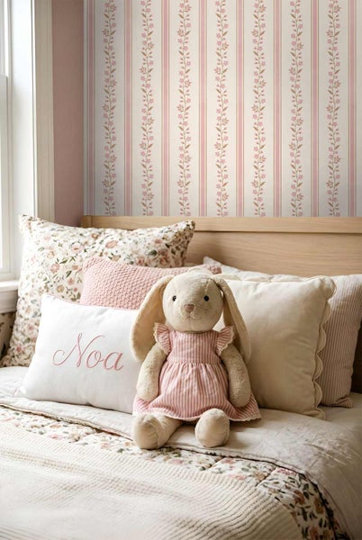 Tapete mit vertikalen Streifen und Blumenranken in einem Kinderzimmer mit Holzbett, Kissen und einem Plüschhasen.