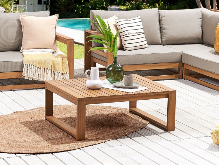 Modernes Garten-Lounge-Set aus Holz mit quadratischem Couchtisch, grauen Sitzkissen und Zierkissen auf einer hellen Holzterrasse.