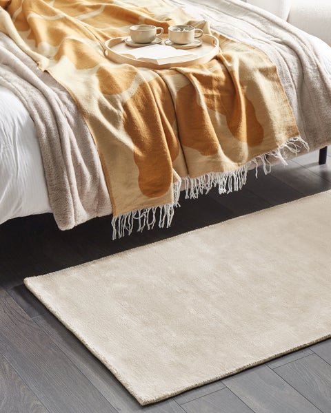 Beige Teppich vor einem Bett mit Decke und Tablett