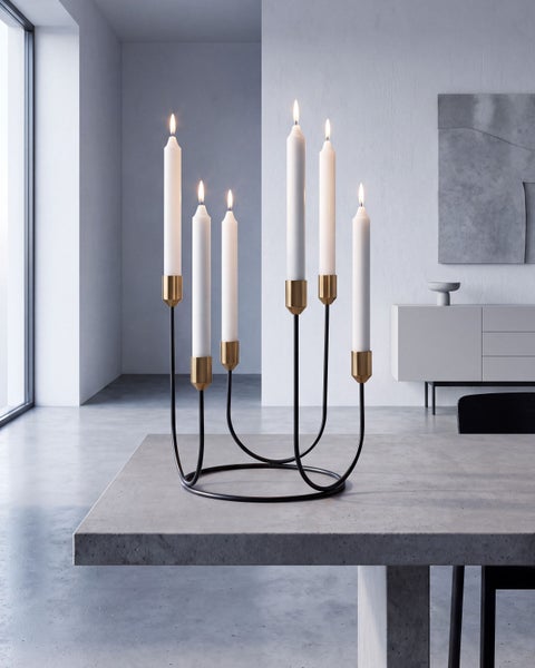 Ein moderner, runder Kerzenständer mit sechs brennenden Kerzen auf einem Betontisch in einem minimalistisch eingerichteten Wohnraum.