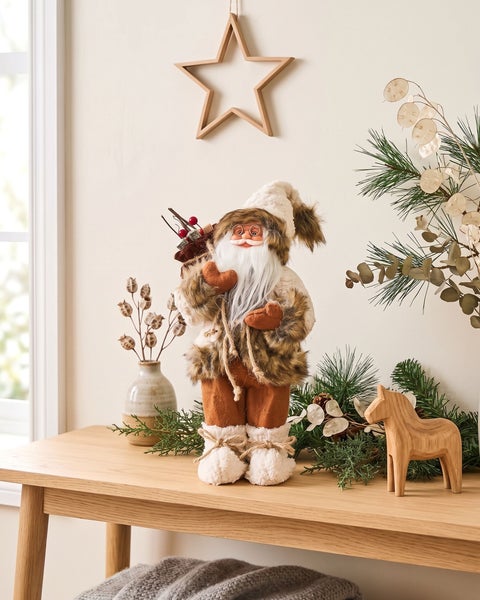 Weihnachtsdekoration Weihnachtsmann Figur mit Kunstfell Kleidung auf einem Holztisch mit Tannenzweigen und Holzstern Wanddekoration.