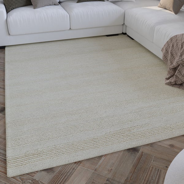 Beiger, rechteckiger Teppich mit Linienstruktur in hellem Wohnzimmer unter weißem Sofa auf Parkettboden.