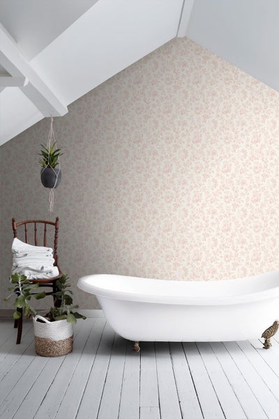 Helles Badezimmer mit floraler Tapete, weißer Badewanne auf Füßen, Holzstuhl mit Handtüchern und Pflanzen auf weißem Dielenboden.