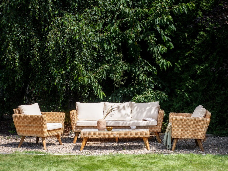 Gartenmöbel-Set mit Rattansofa, Rattansesseln und Rattantisch auf Rasen vor Büschen