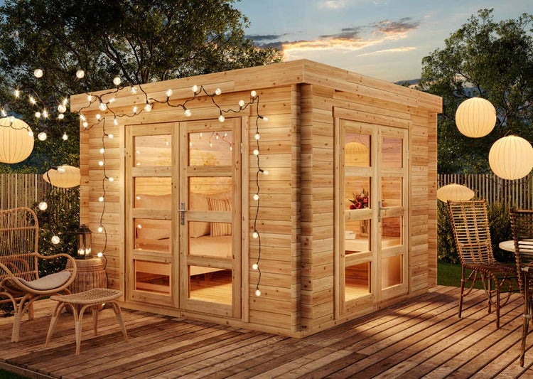 Modernes Gartenhaus aus Holz mit Flachdach und großen Glastüren auf einer Holzterrasse in einem beleuchteten Garten.