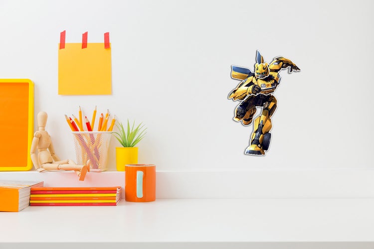Wandsticker Transformers Bumblebee in einem hellen Kinderzimmer über einem Schreibtisch mit Schreibutensilien und Holzgliederpuppe.