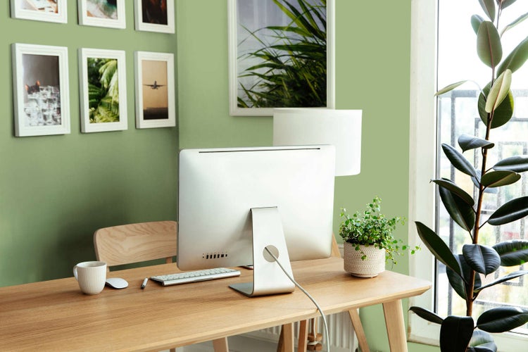 Modernes Arbeitszimmer mit Schreibtisch aus Holz, Computer, Tischlampe, Wandbildern und Zimmerpflanzen.