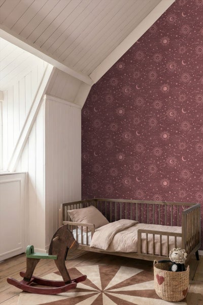 Helles Kinderzimmer mit gemusterter Tapete mit Sonnen und Mondmotiven, Kinderbett aus Holz und Schaukelpferd unter einer Dachschräge.