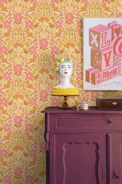 Dekoratives Interieur mit gemusterter Tapete, bemalter Kommode und dekorativen Gegenständen