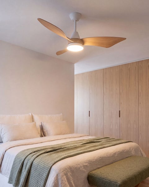 Ein Deckenventilator mit Beleuchtung und drei geschwungenen Holzflügeln über einem modern eingerichteten Schlafzimmer mit einem großen Holzschrank.