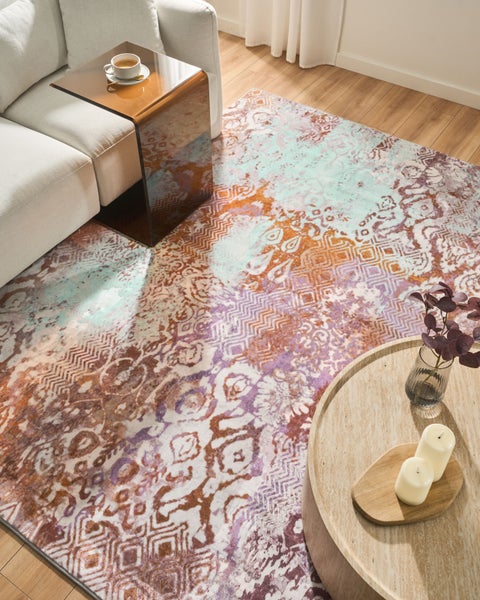 Gemusterter Teppich mit Vintage-Motiven in einem hellen Wohnzimmer mit Sofa und Couchtisch auf Holzboden.