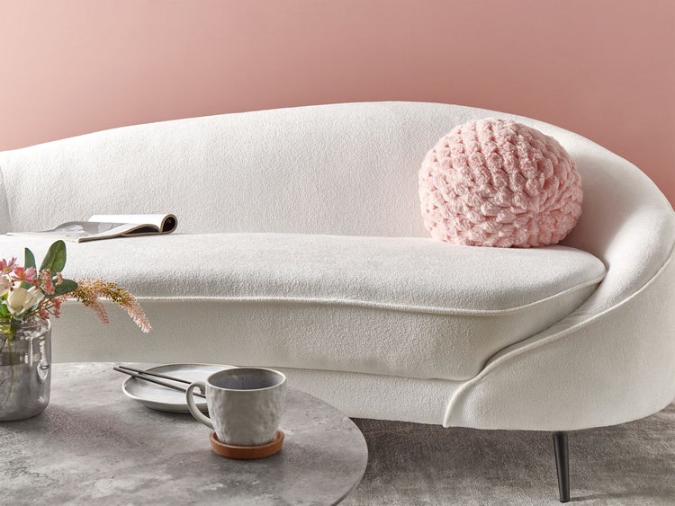 Szene mit weißem Sofa, Dekokissen, Tisch mit Blumenvase, Tasse, Teller und Buch.