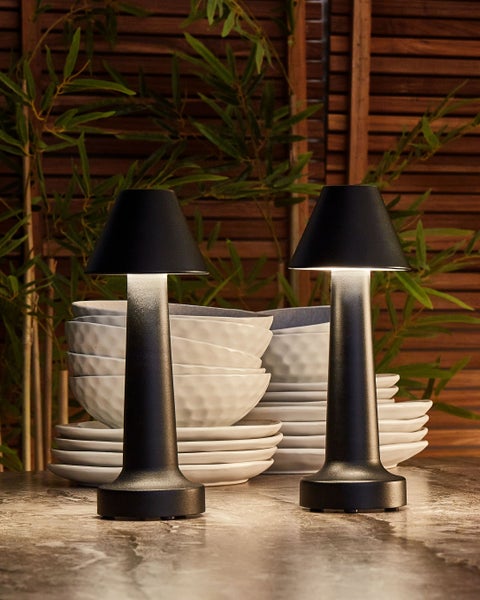 Zwei kabellose Tischleuchten neben Geschirr auf einem Tisch