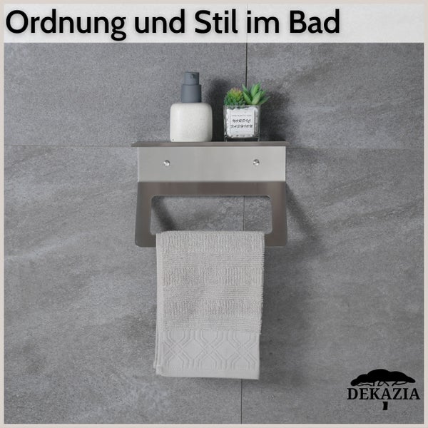 Wandmontierter Handtuchhalter aus Edelstahl mit Ablagefläche für Badutensilien auf einer Fliesenwand. Dekazia Logo.