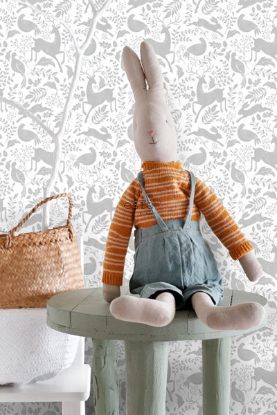 Dekorative Szene mit Stoffhase auf einem kleinen Tisch vor einer Tapete mit Tiermotiven