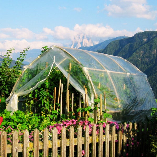 Gewächshaus im Garten mit Holzzaun im Vordergrund und Berglandschaft im Hintergrund